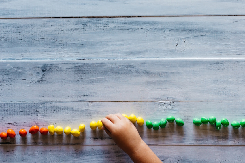 farbene perlen, kleine perlen, holzoberfläche, kinderhand, taktile spielperlen
